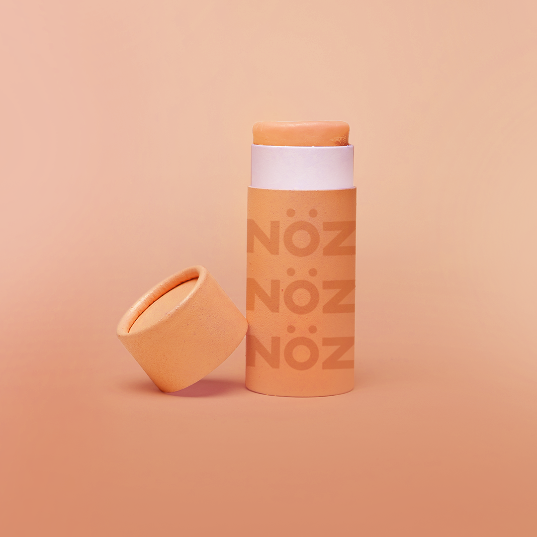 Light red NÖZ reef safe sunscreen with cap removed and tilted on base.